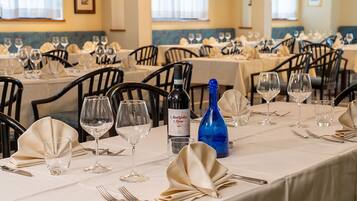 Un restaurant où de nombreuses tables sont dressées pour le dîner, chacune étant agrémentée de verres à vin, de couverts et d’une bouteille de vin.
