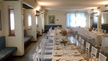 A long dining table set with white chairs, a bench, and a wall-mounted sofa.