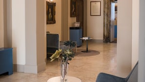 A spacious lobby with high ceilings, a round table with a vase, a blue sofa, and framed artwork on the walls. - Hotel Bosone Palace (Gubbio)