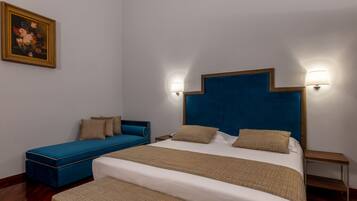 A bedroom with a large bed, a blue sofa, two bedside tables, and a wall-mounted lamp.