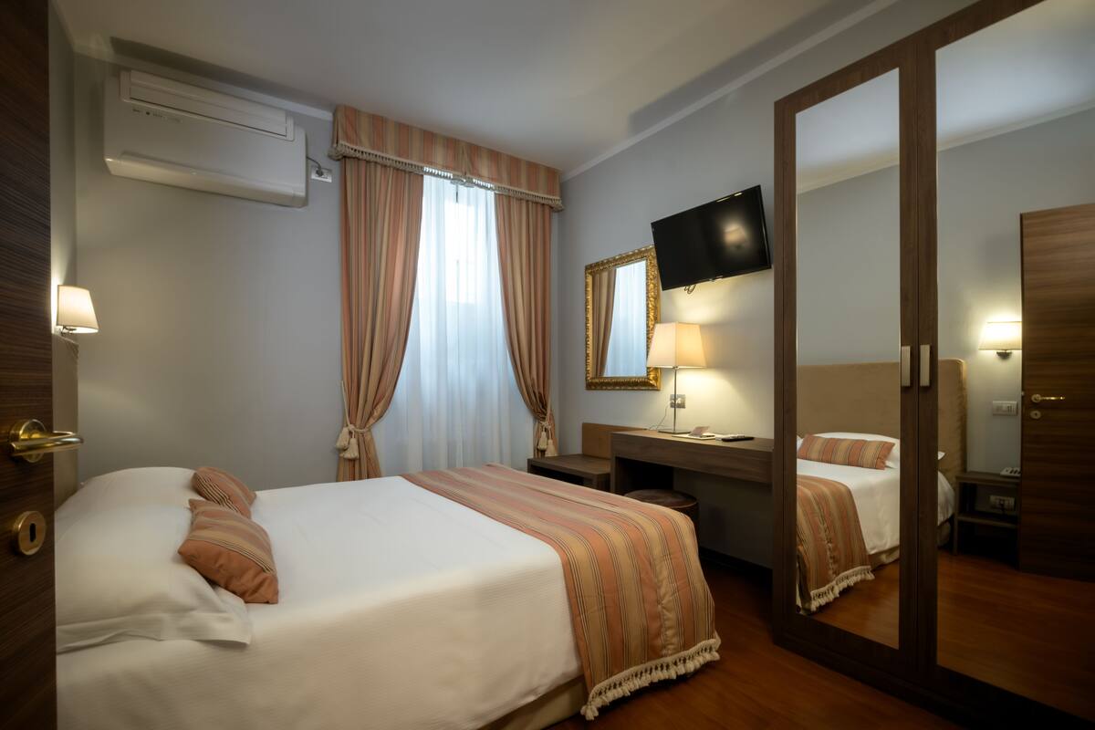 Hotellihuone, jossa on sänky, yöpöytä, lamppu, televisio ja peili.