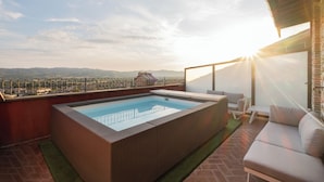 A rooftop pool with a view of distant mountains, a seating area with a sofa and chairs, and a glass railing. - Hotel Bosone Palace (Gubbio)