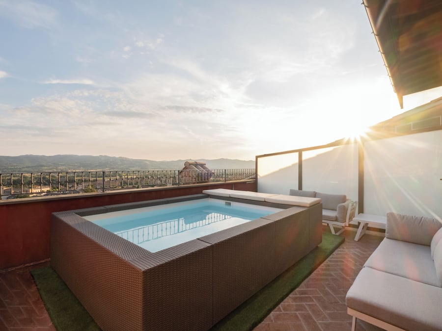 A rooftop pool with a view of distant mountains, a seating area with a sofa and chairs, and a glass railing.