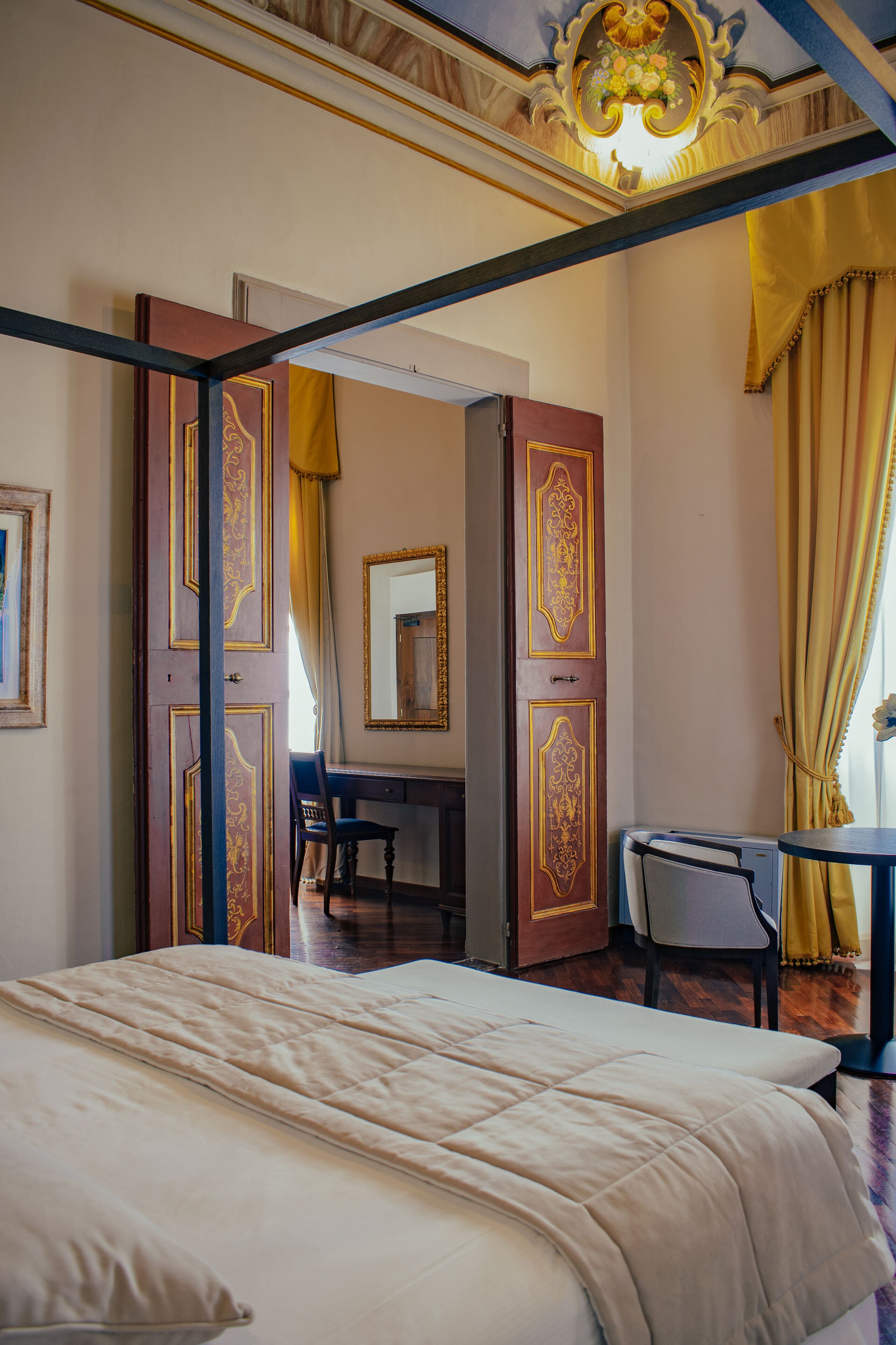 Una habitación con una cama, un escritorio y una silla, con puertas ornamentadas y un candelabro.