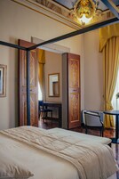 Una habitación con una cama, un escritorio y una silla, con puertas ornamentadas y un candelabro.