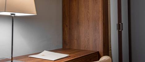 A small office space with a wooden desk, a chair, a lamp, and a flat-screen TV mounted on the wall.