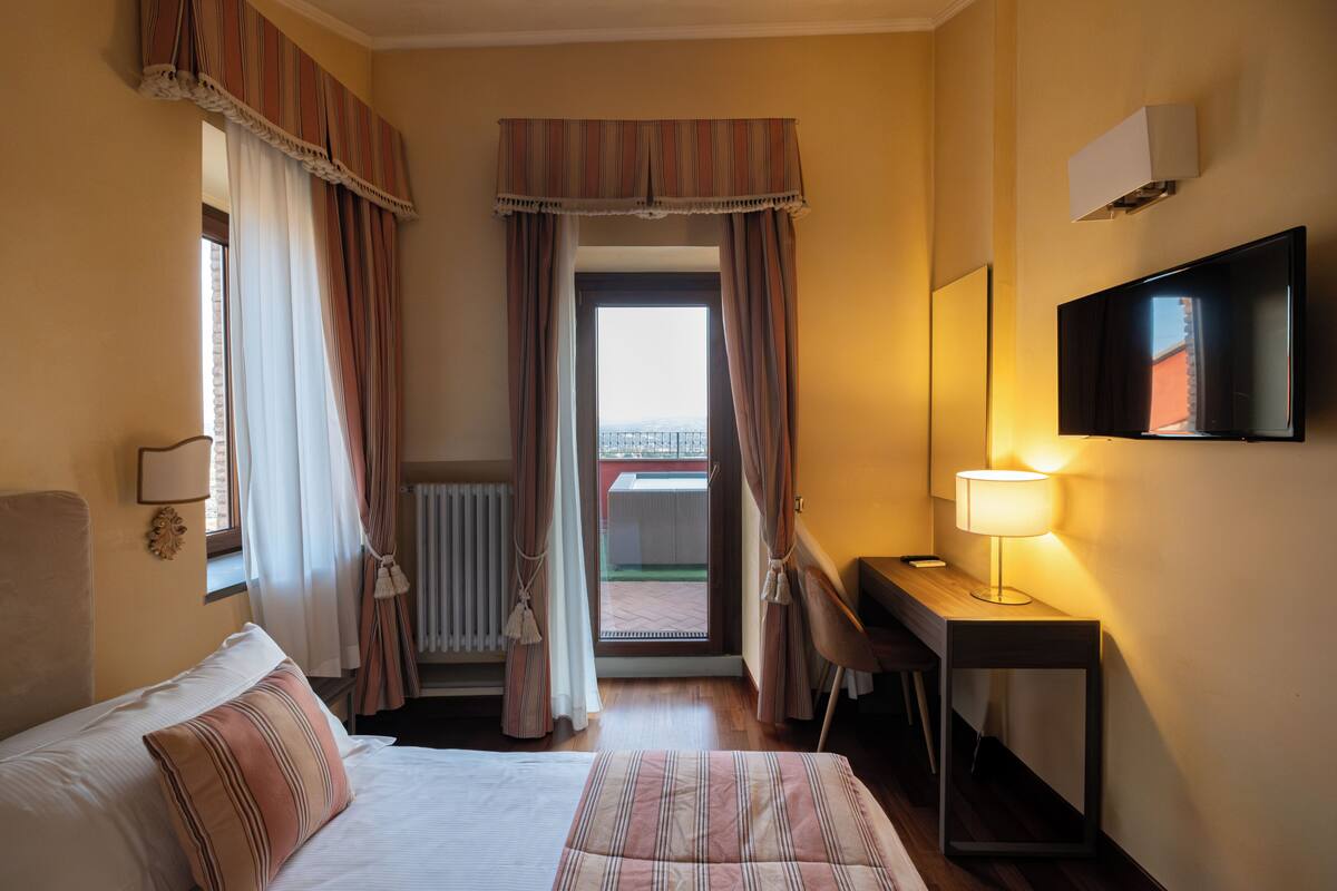 Hotellihuone, jossa on sänky, työpöytä, tuoli, televisio ja ikkuna, jossa on verhot.