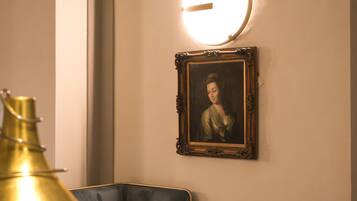 A room with a sofa, a small round table with a book, a gold-colored vase, and a framed painting on the wall.