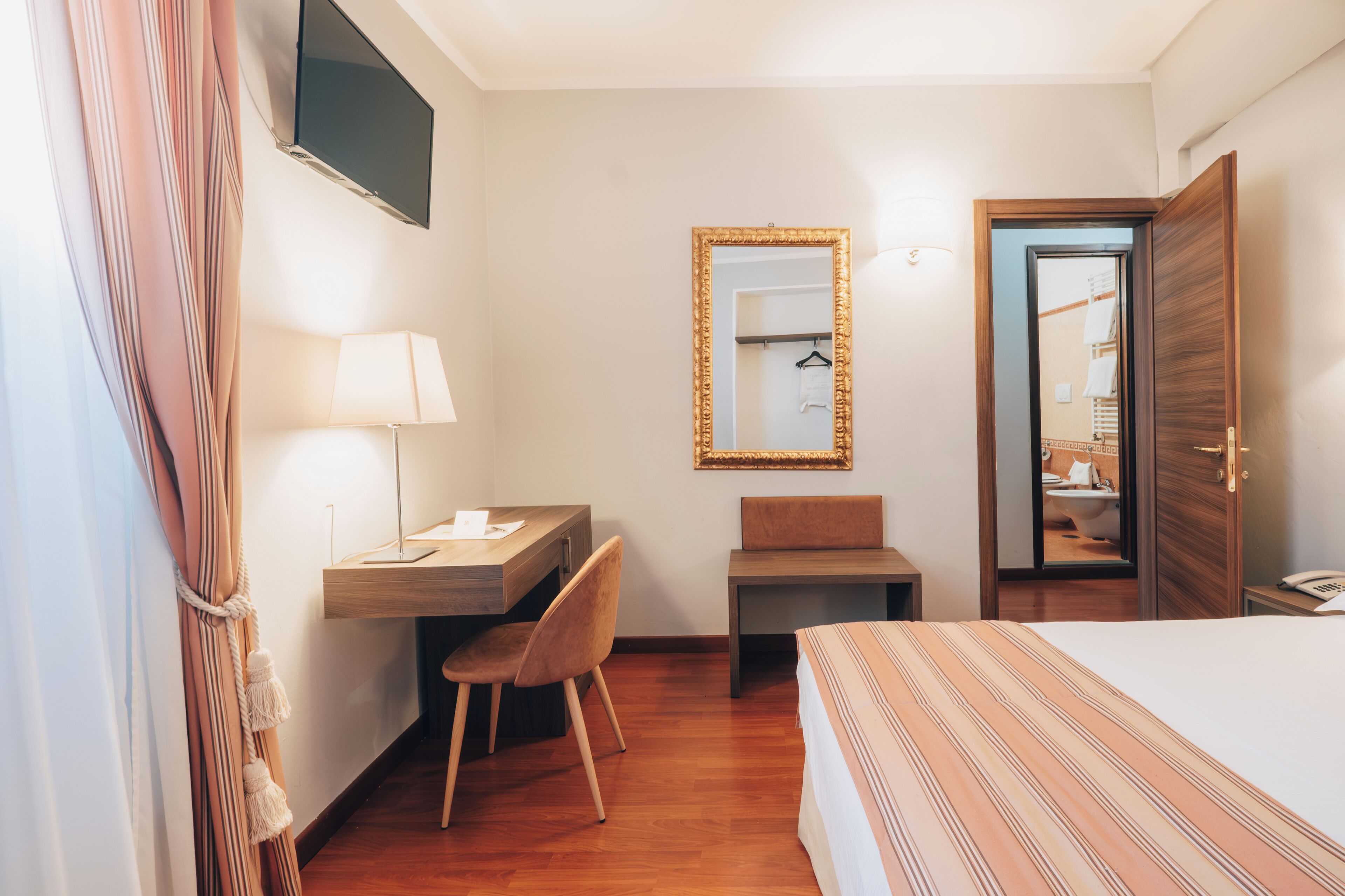 A hotel room with a bed, desk, chair, and a mirror.