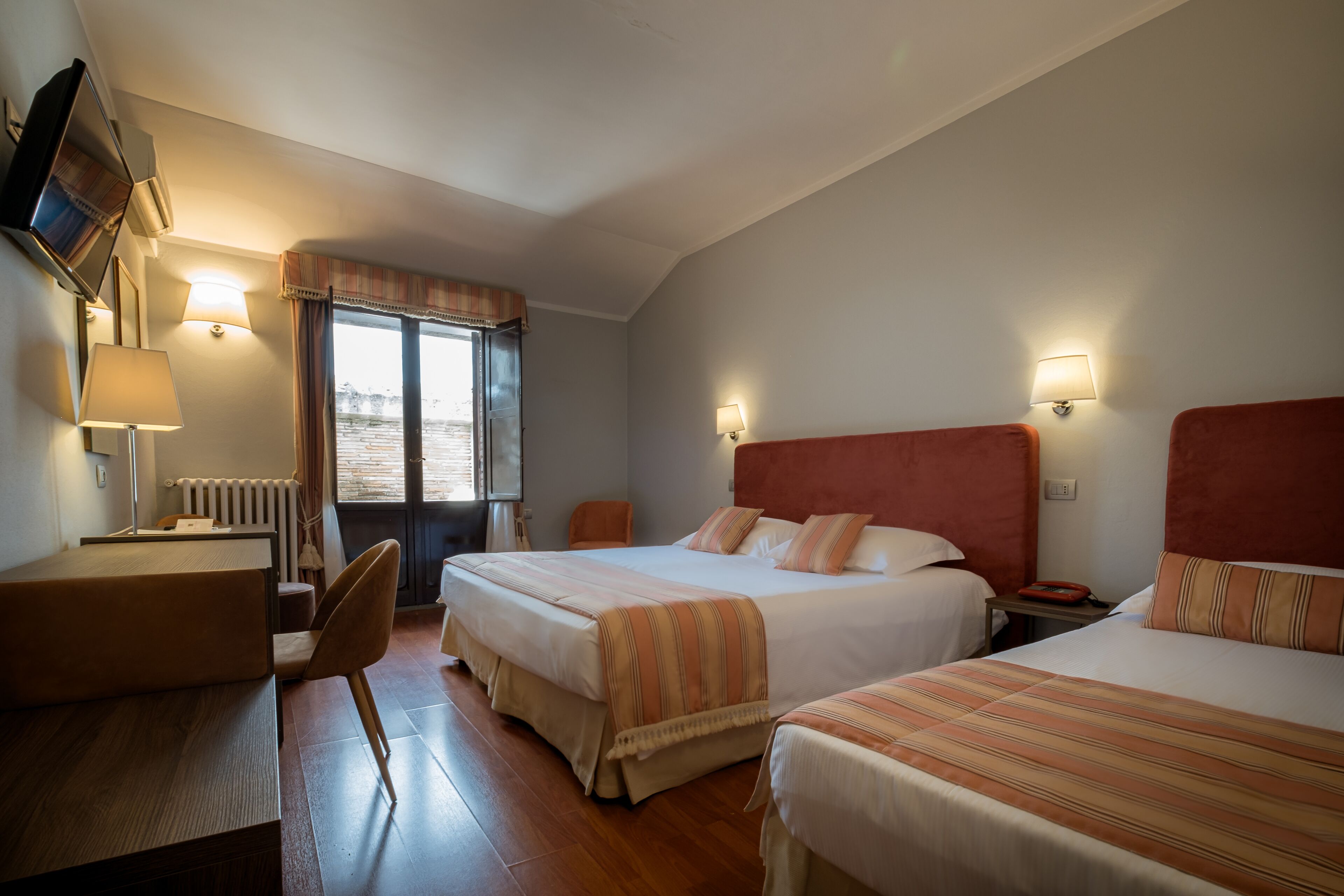Ein Hotelzimmer mit zwei Betten, einem Schreibtisch, einem Stuhl und einem Fenster mit Vorhängen.