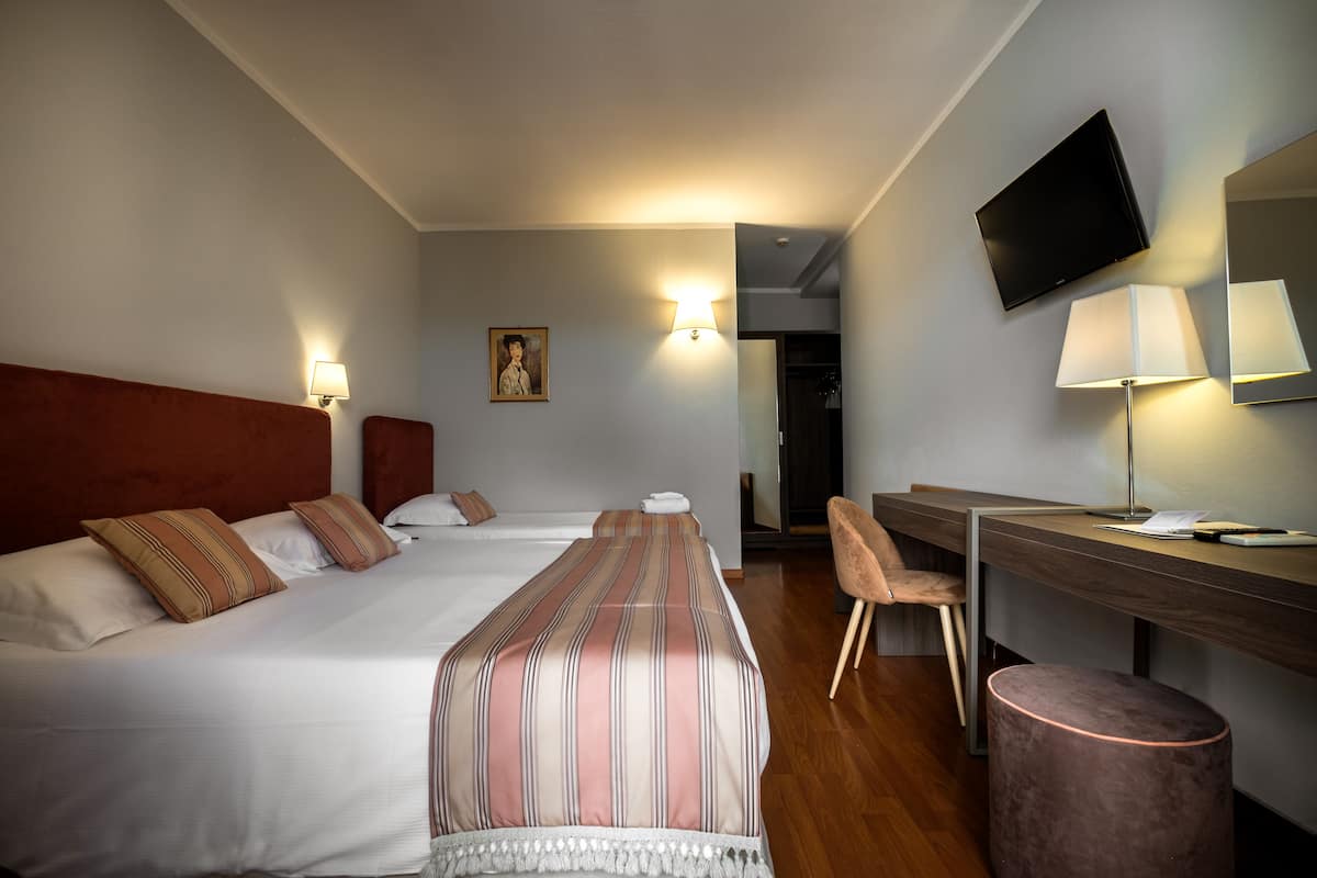 Hotellihuone, jossa on kaksi sänkyä, työpöytä, tuoli, televisio ja lamppu.