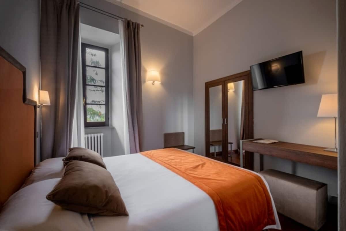 Hotellihuone, jossa on sänky, työpöytä, tuoli, televisio ja ikkuna, jossa on verhot.