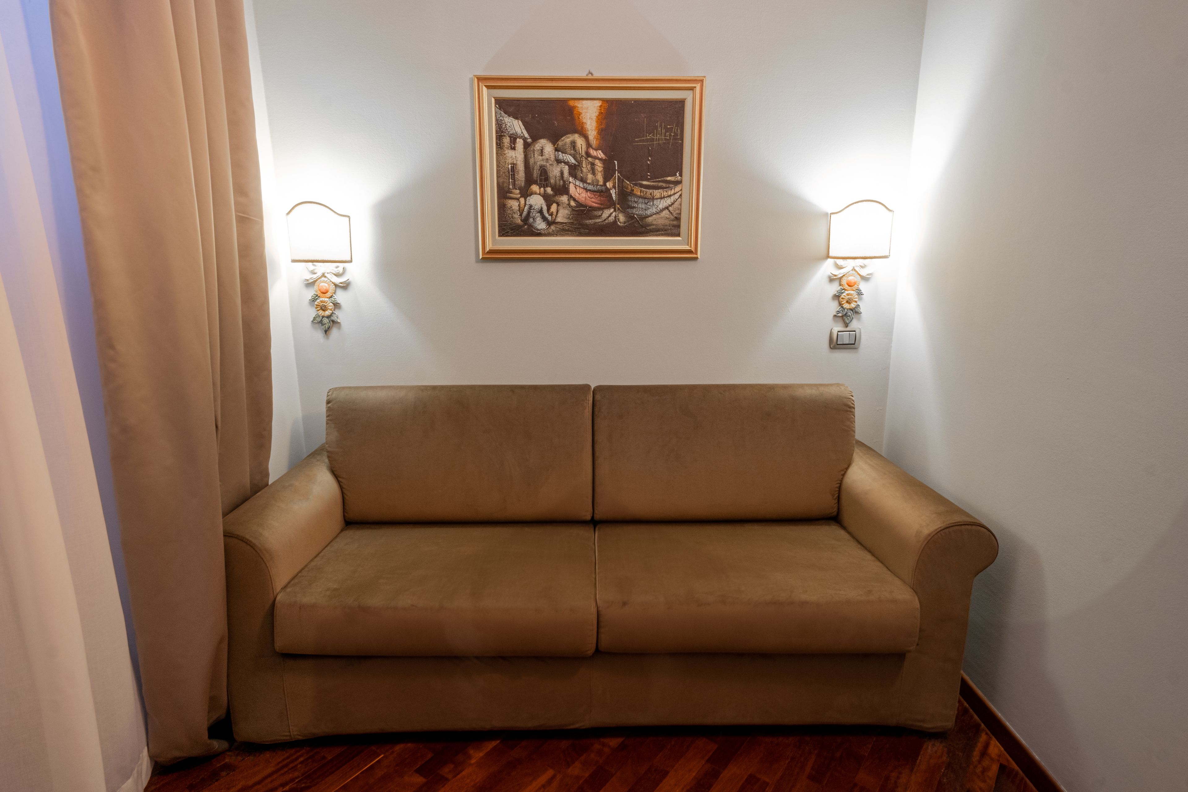 Une pièce avec un canapé beige, un tableau encadré accroché au mur et deux appliques murales.