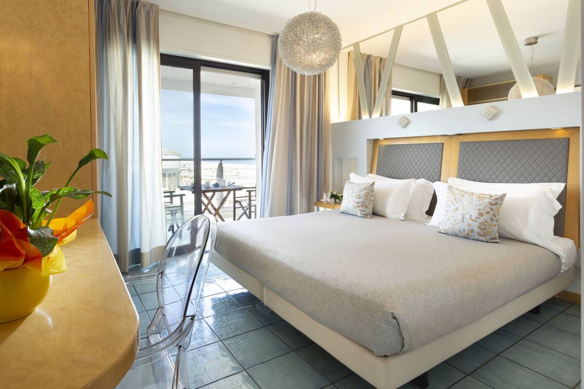 A hotel room with a large bed, a balcony with a table and chairs, and a view of the city.
