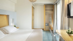 Ein Hotelzimmer mit einem Bett, einem hölzernen Kopfteil, einem Nachttisch mit Blumenvase und einer Schiebetür zum Badezimmer.