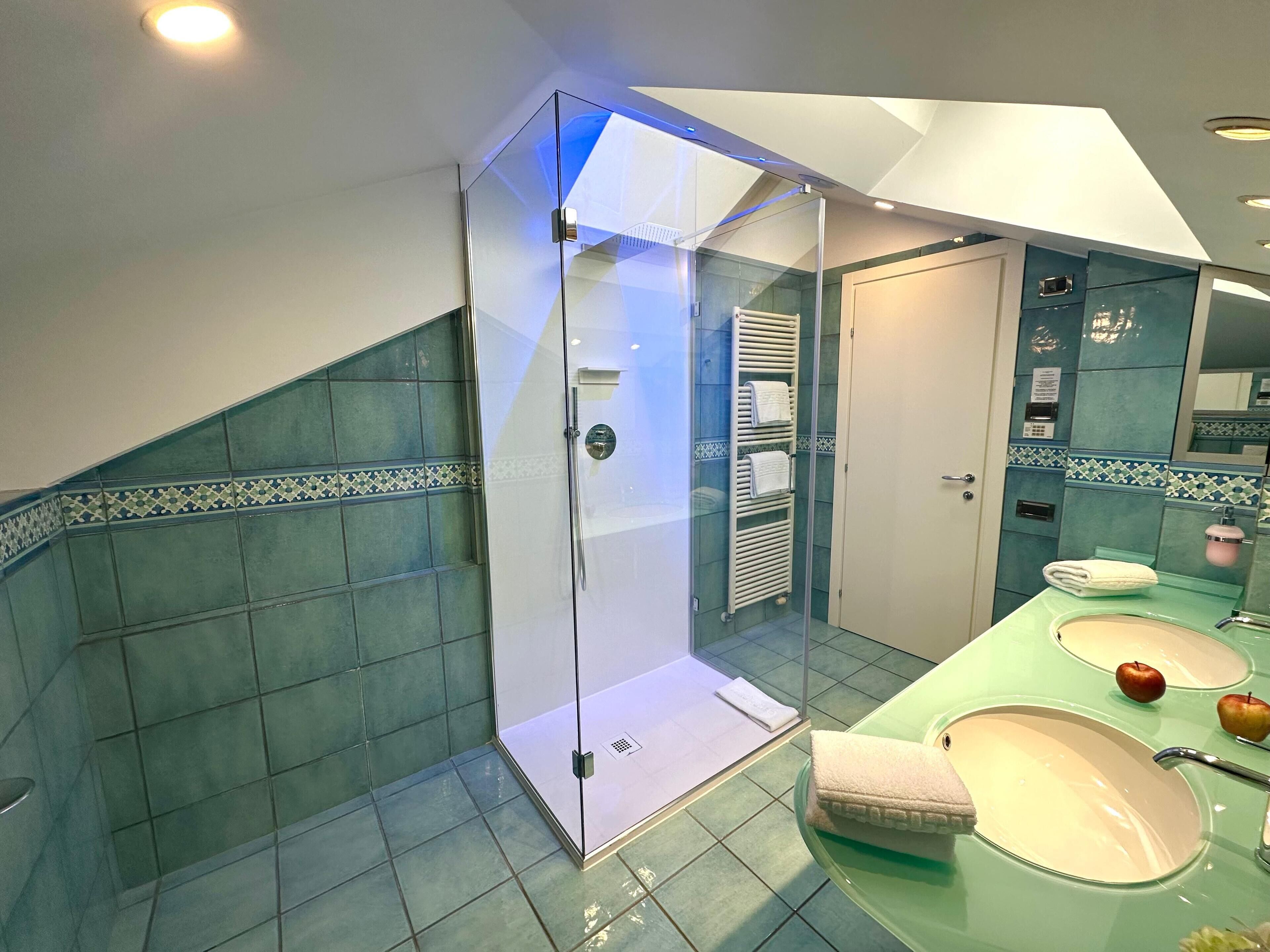 Un bagno moderno con doccia a vetro, un mobile lavabo con due lavandini e uno specchio con illuminazione integrata.
