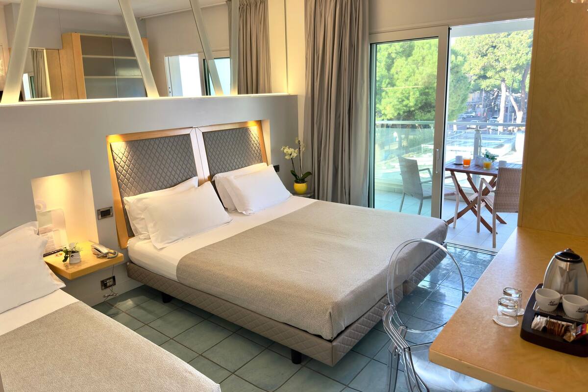A hotel room with a large bed, bedside tables, a desk with a coffee maker, and a view of the outdoors.