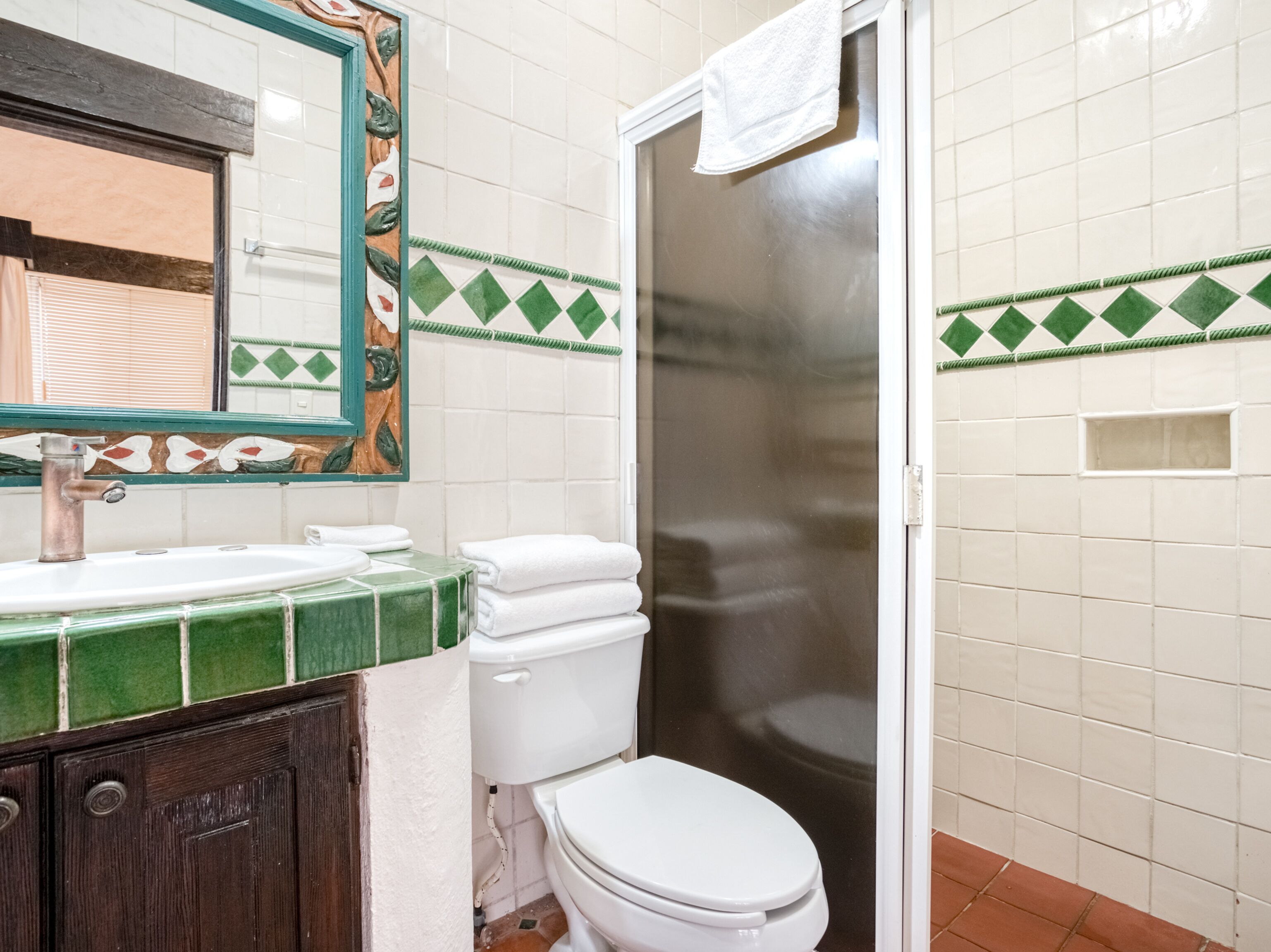 A bathroom with a white toilet, green-tiled sink, and a mirror with a decorative frame.