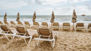 A beach with rows of white lounge chairs and beige umbrellas. - Capital O Mimi Del Mar, Playa del Carmen (Playa del Carmen)