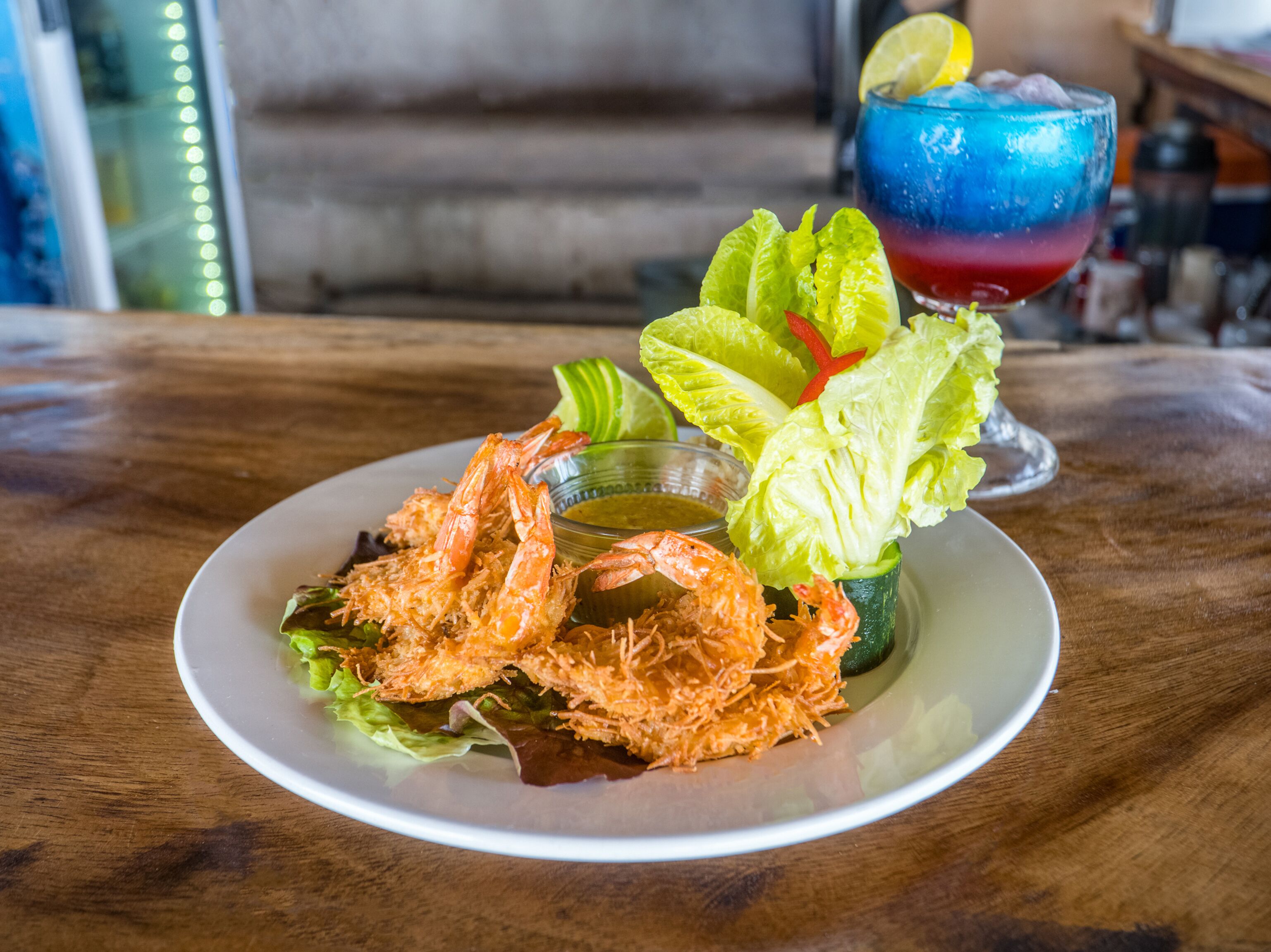A plate of fried shrimp with lettuce and a cocktail in a glass.