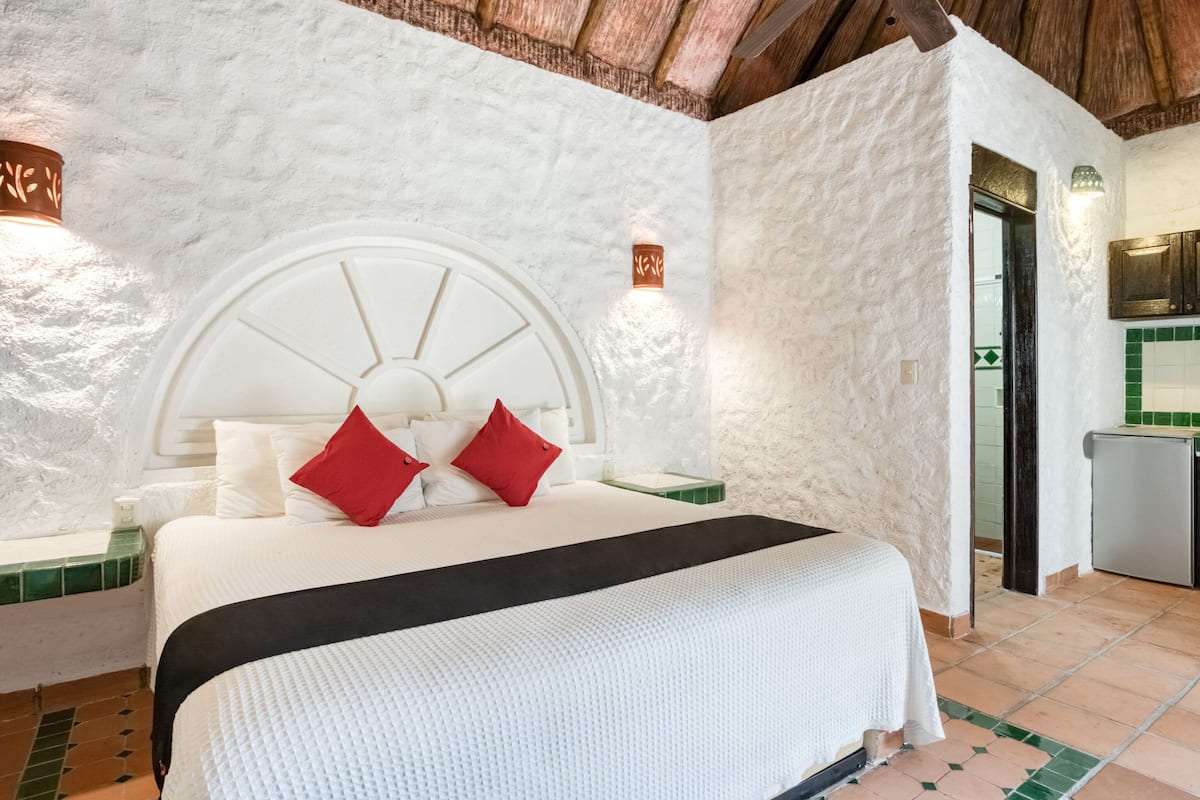 Een slaapkamer met een wit bed, rode kussens, een wit hoofdeinde en een vloer met groene en witte tegels.