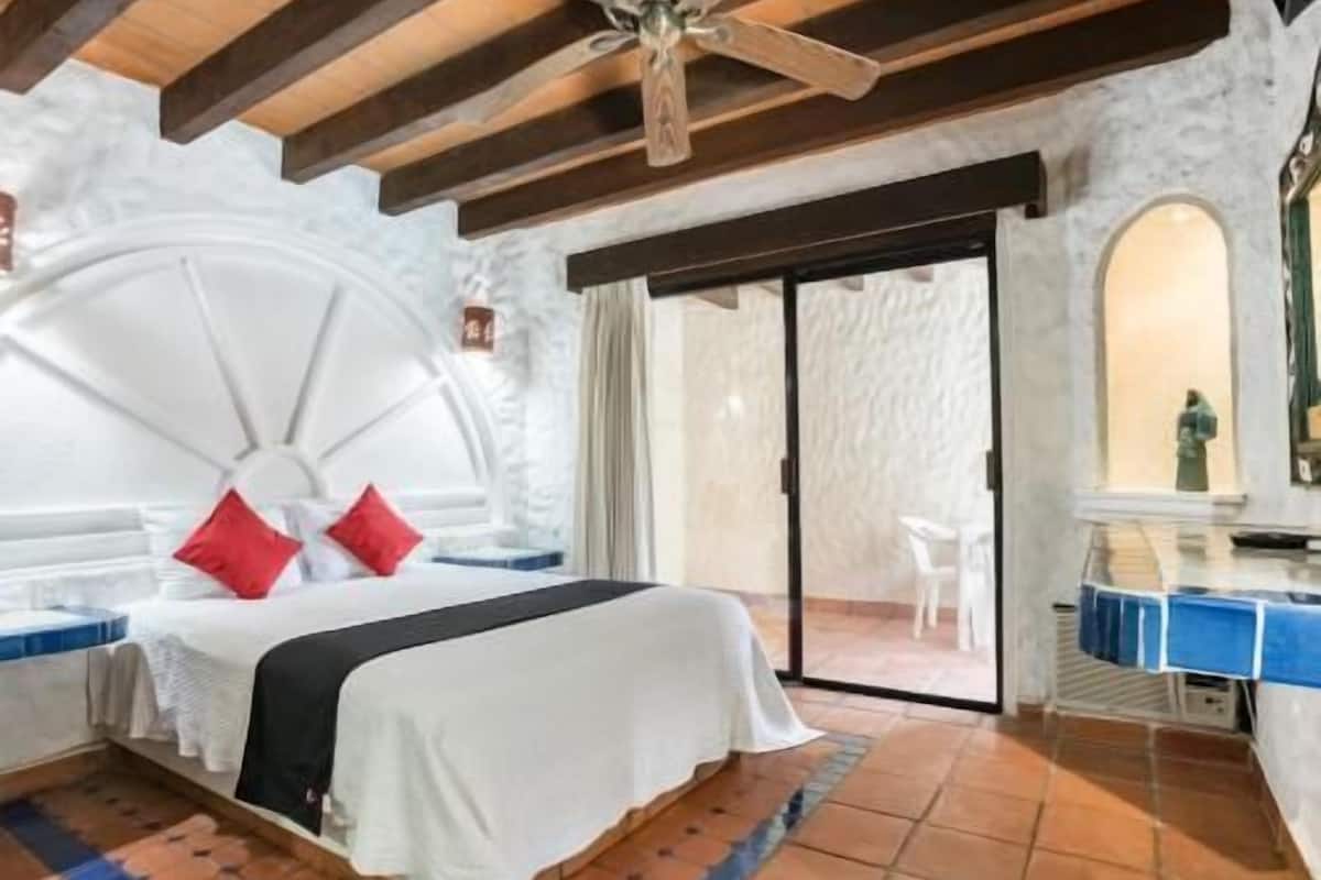 Een slaapkamer met een bed, een plafondventilator, een schuifdeur en een zichtbare badkamer.