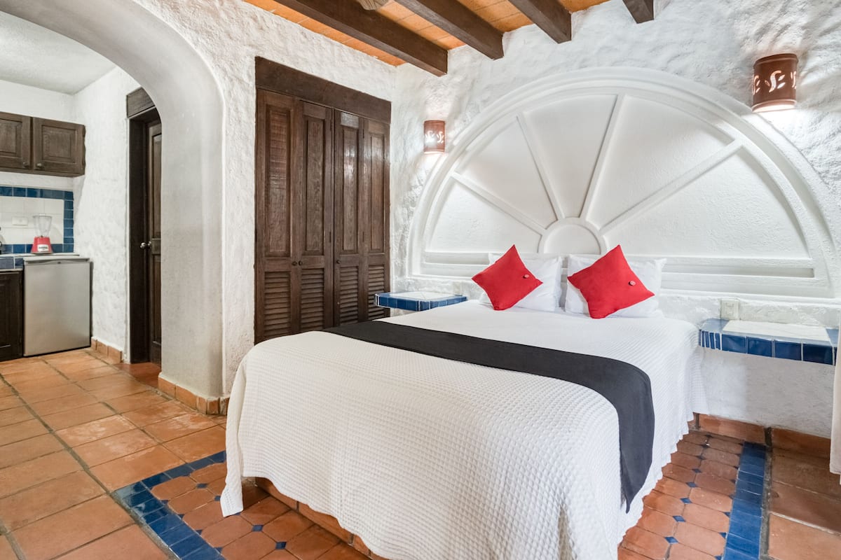 Een slaapkamer met een groot bed, een houten garderobe en een keukenhoek met een blender.