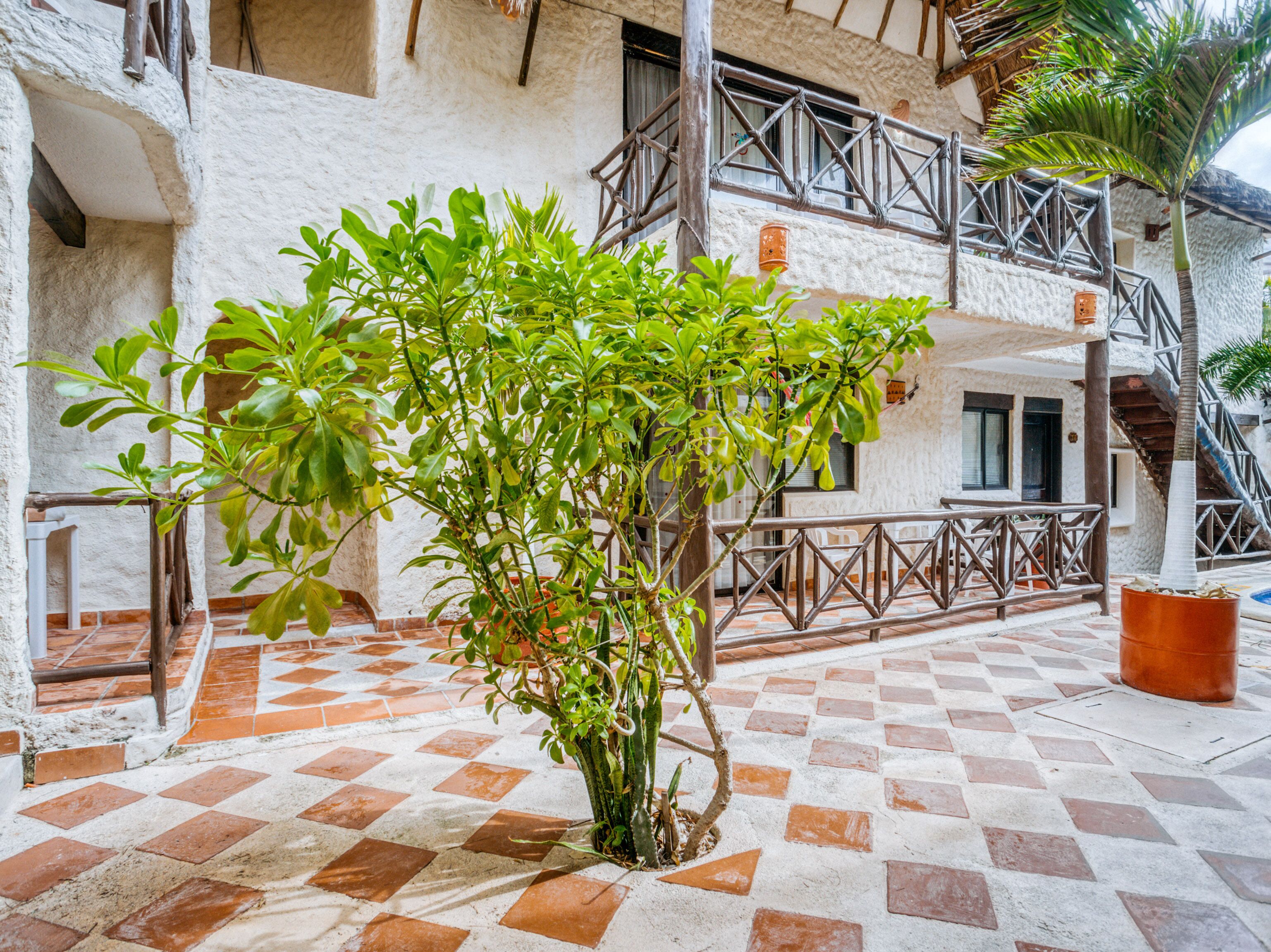 Une cour avec un sol à carreaux, un arbre et un bâtiment doté d’un balcon.