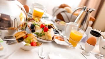 Un desayuno con diversos platos, como huevos, tostadas y fruta, sobre una mesa blanca con cubiertos y una cafetera.