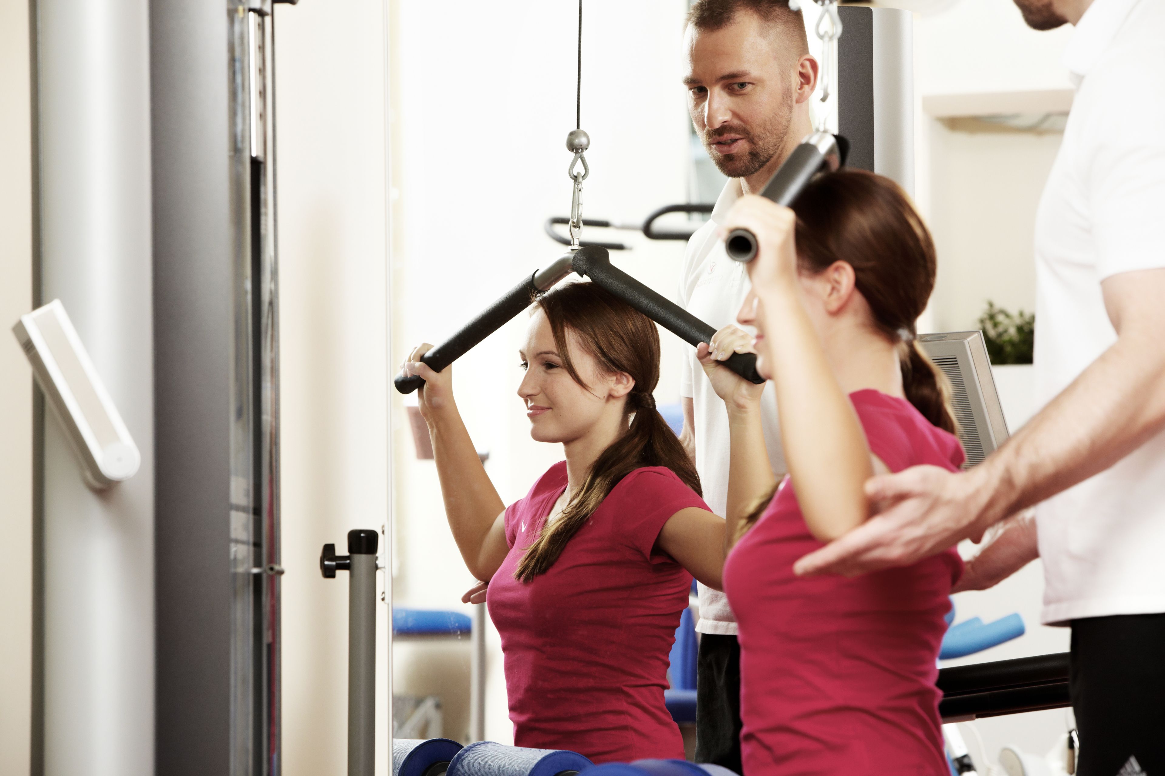 A gym with exercise equipment and a person assisting another person.