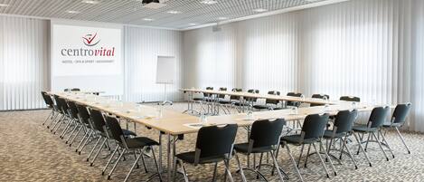 A conference room with a long table, chairs, a projector, and a presentation screen with the logo "centrovital".