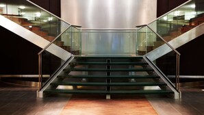 Un escalier moderne avec des rampes en verre et des marches en bois, menant à un étage supérieur.