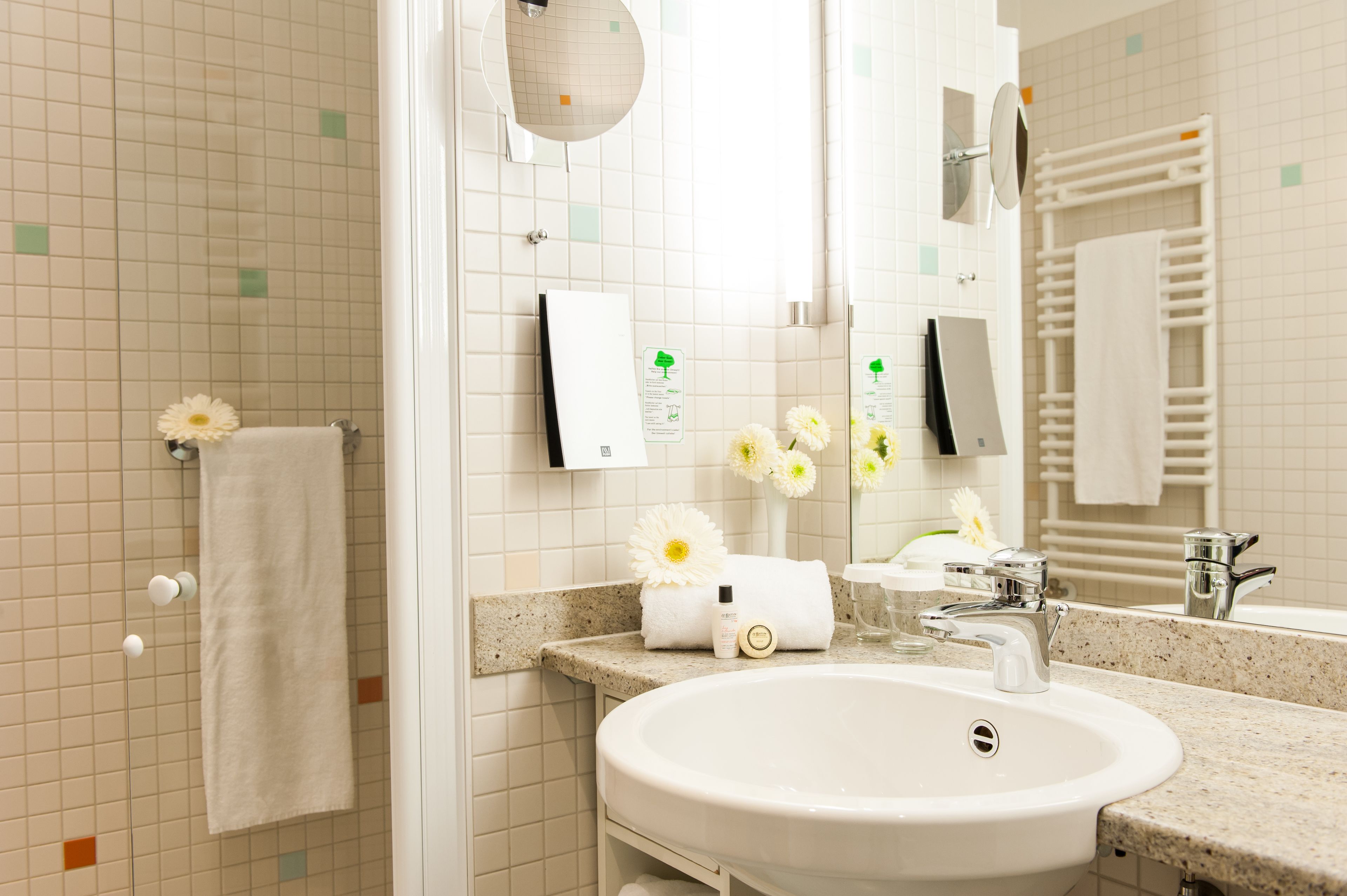 Un baño con lavamanos, espejo, toallero y un arreglo floral.