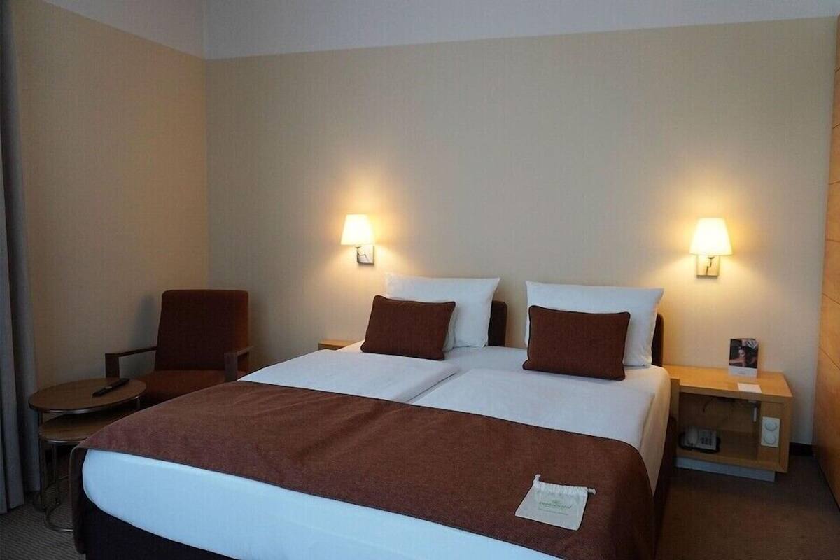 Une chambre d’hôtel avec un grand lit, deux tables de chevet, une chaise et deux lampes fixées au mur.
