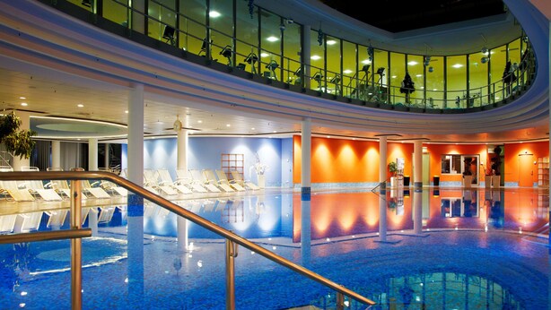 Une grande piscine intérieure dotée d’une balustrade en verre, de chaises longues et d’une terrasse supérieure incurvée avec des sièges.
