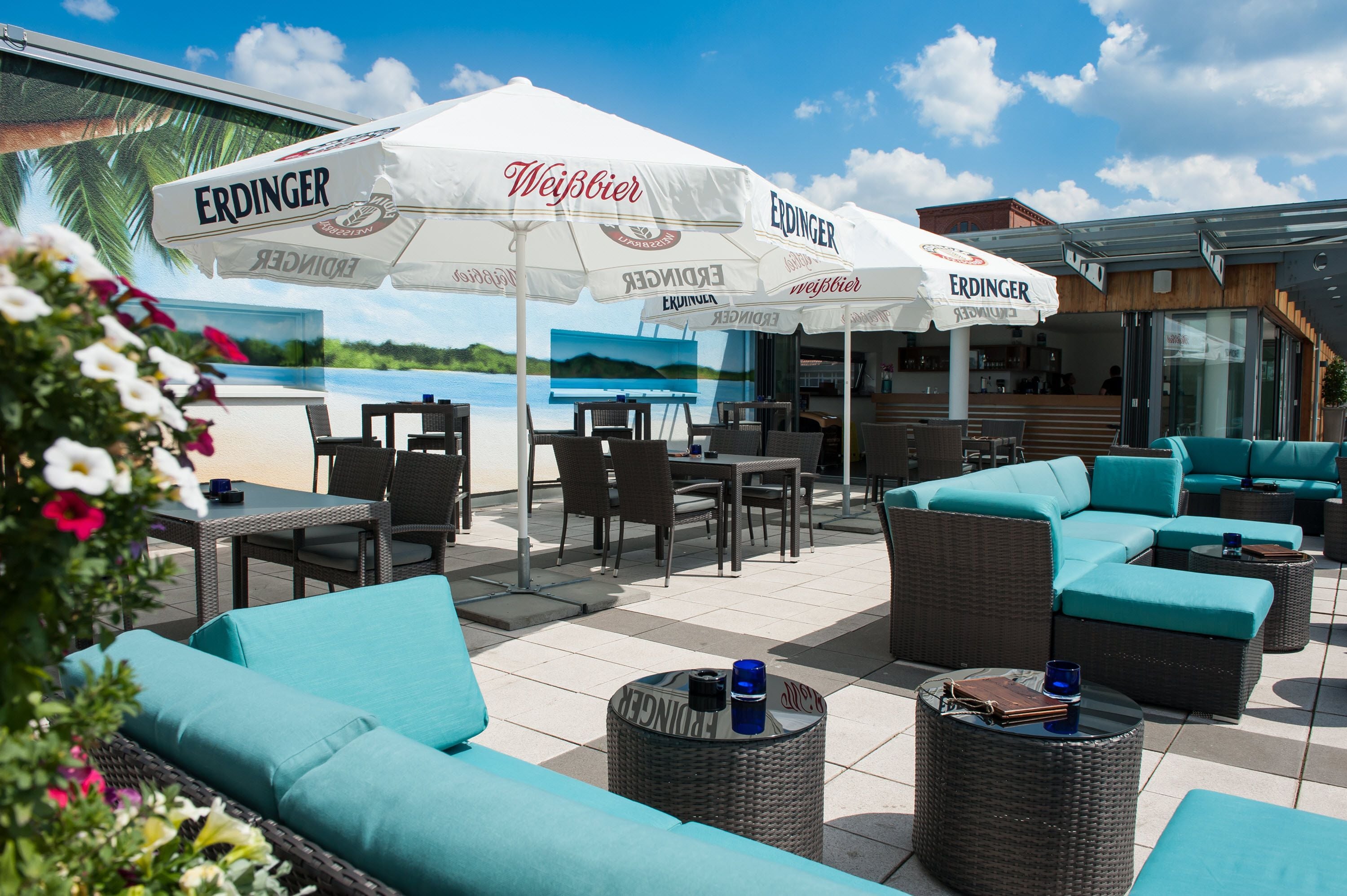 An outdoor seating area with wicker furniture and umbrellas labeled 'ERDINGER'.