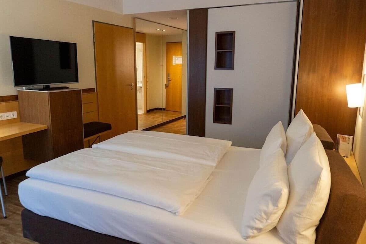 Une chambre d’hôtel équipée d’un lit, d’un bureau, d’une télévision et d’un miroir.