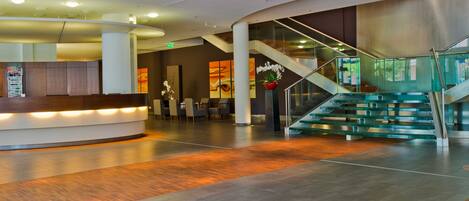 A modern lobby with a reception desk, seating area, and a staircase with glass railings.
