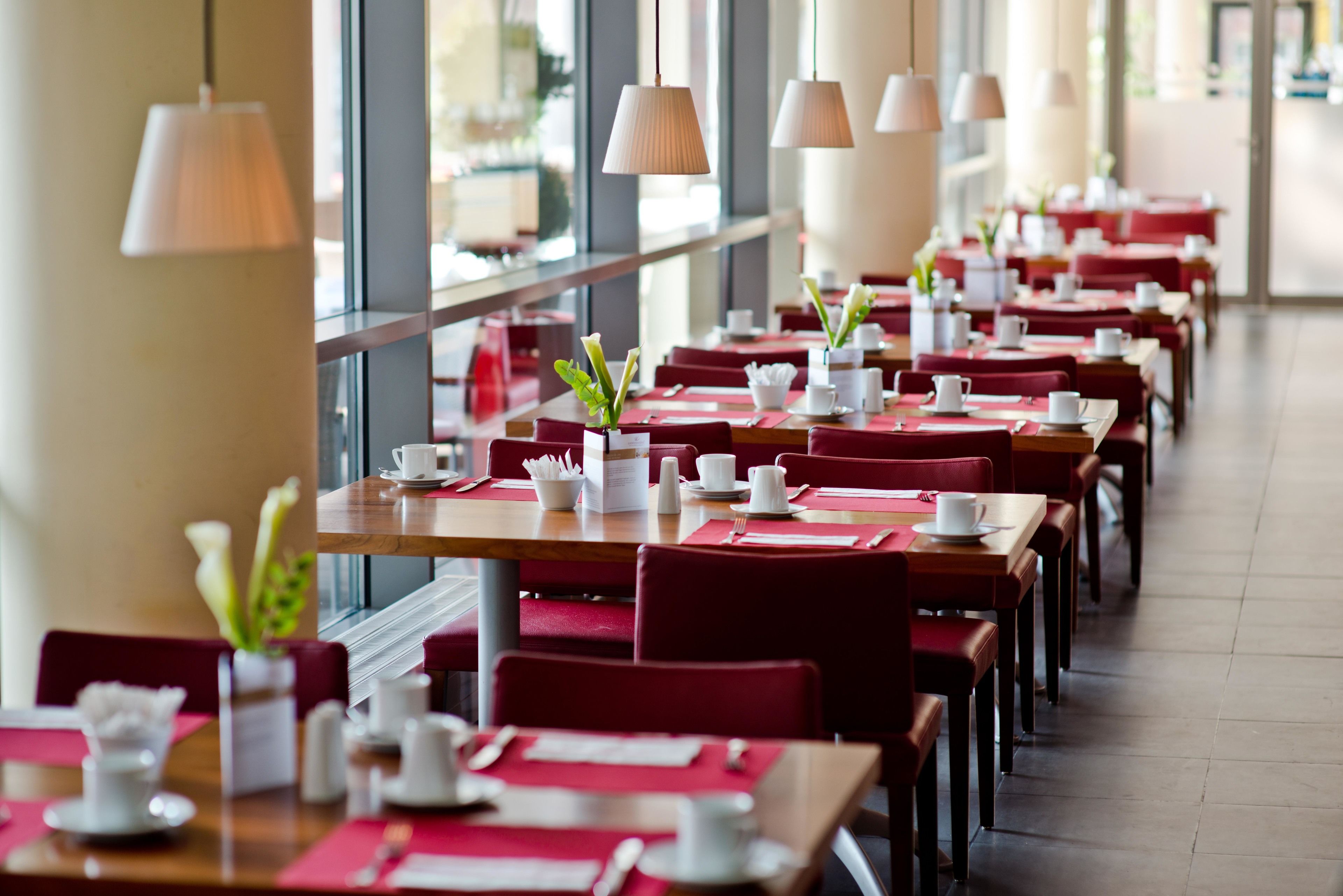 A restaurant with red chairs and tables, white tableware, and hanging lamps.