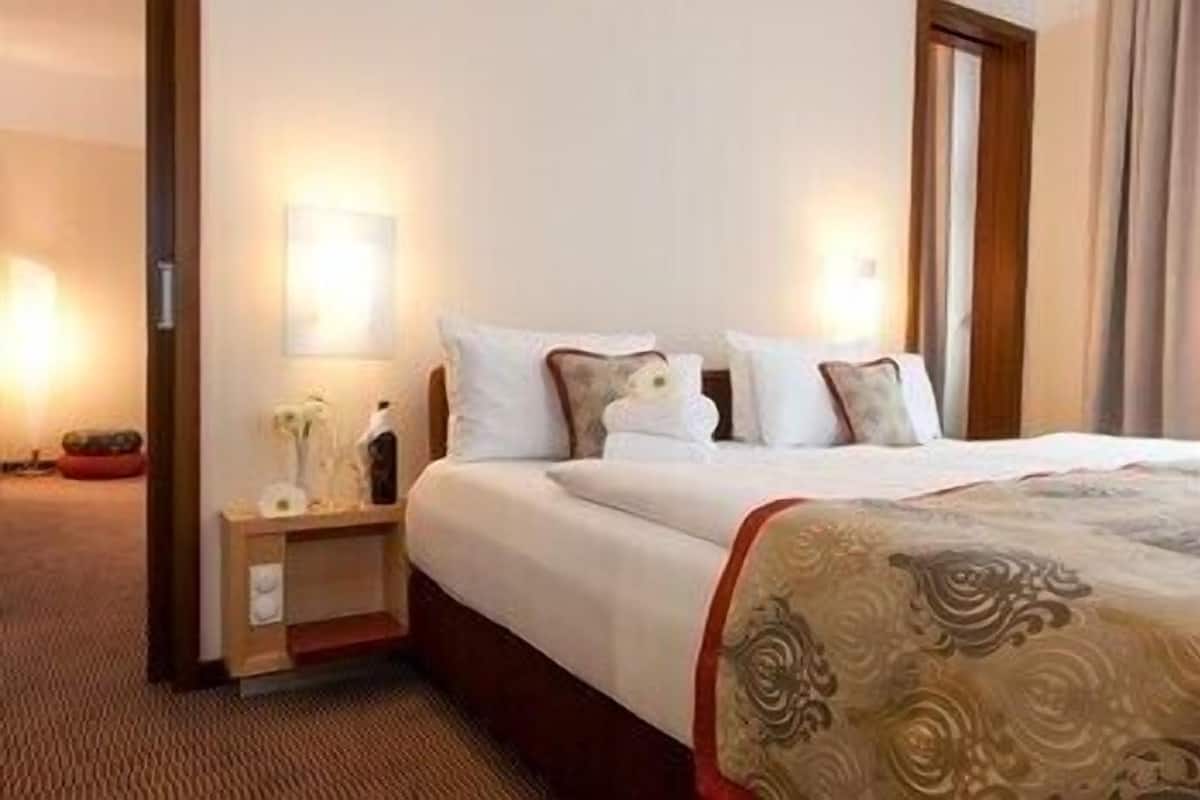 Een hotelkamer met een netjes opgemaakt bed, een nachtkastje met een lamp en een groot raam met gordijnen.