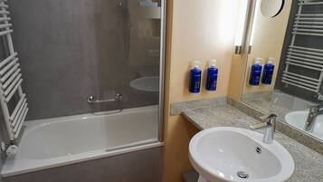 Un baño con bañera, lavamanos y espejo. Hay dos botellas azules en la pared.