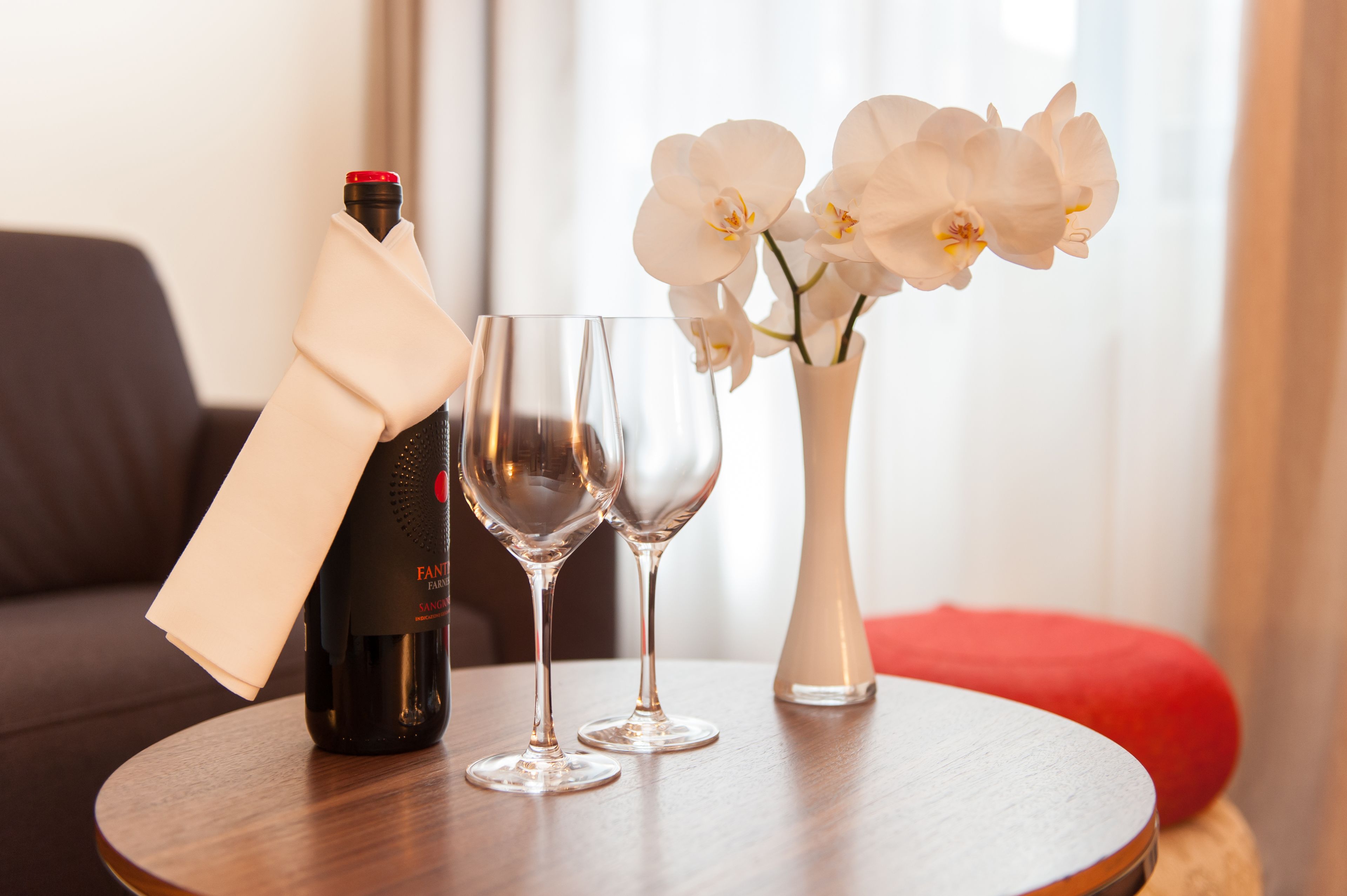 A table with a bottle, two glasses, and a vase with flowers.