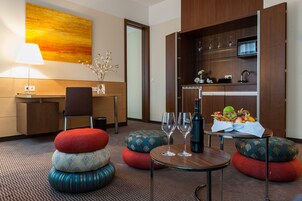 Ein Hotelzimmer mit Essbereich, einer Sofagarnitur, einem Tisch mit Weingläsern und einer Obstschale.