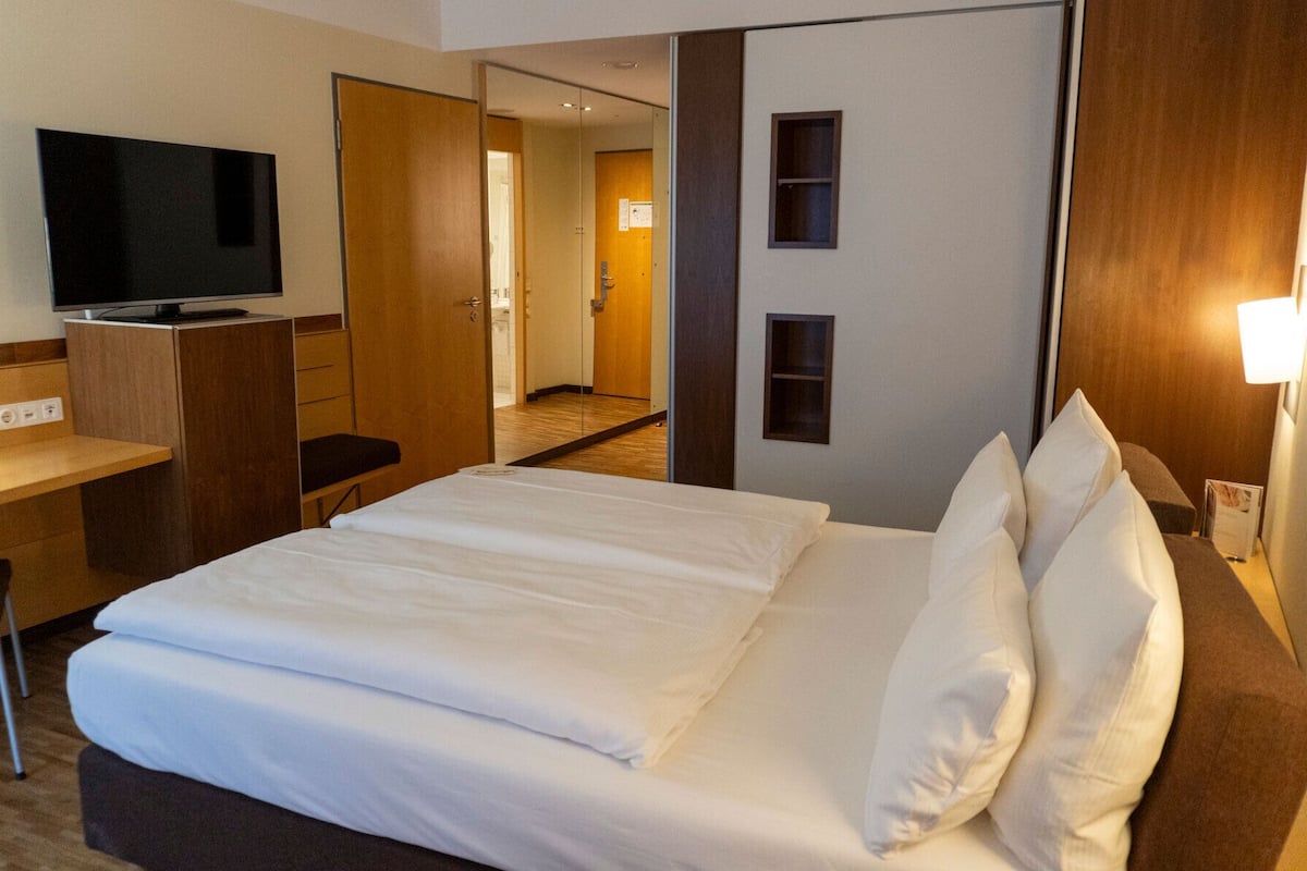 Une chambre d’hôtel comprenant un lit, un bureau avec une télévision, une chaise et une porte donnant sur une salle de bain.
