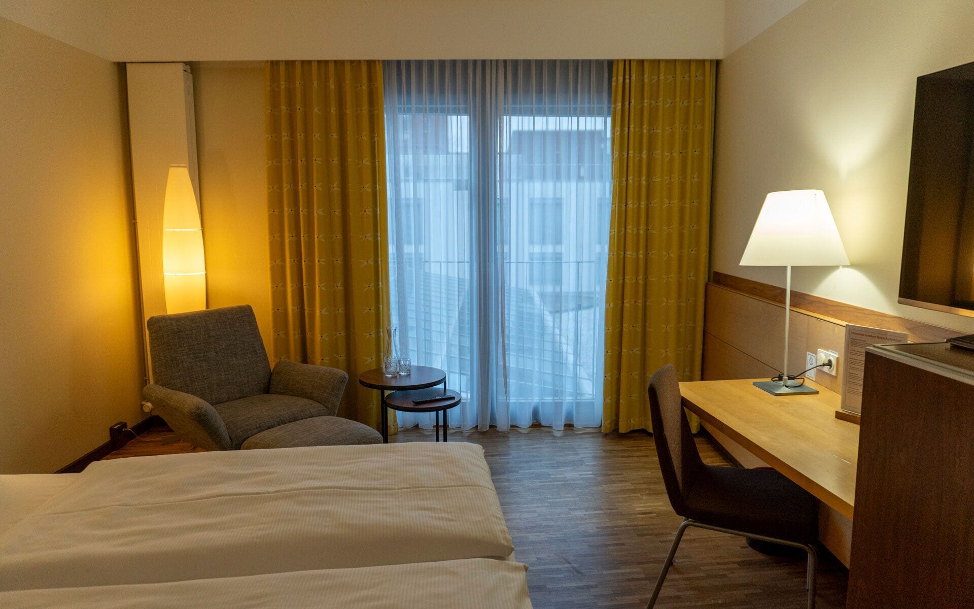 Hotellihuone, jossa on sänky, työpöytä, tuoli, pieni pöytä ja lamppu.