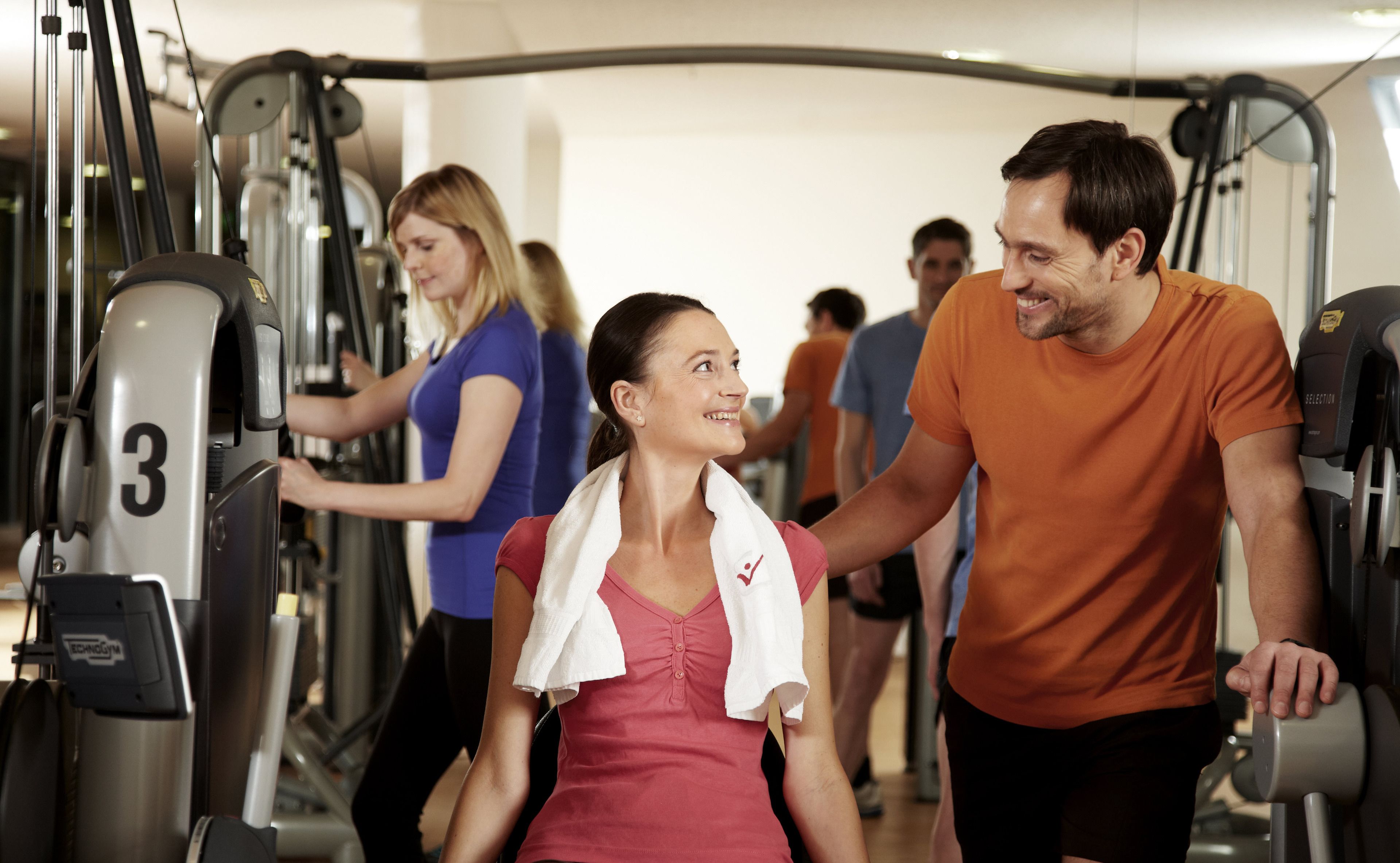 Een sportschool met trainingsapparatuur en mensen die aan het sporten zijn.
