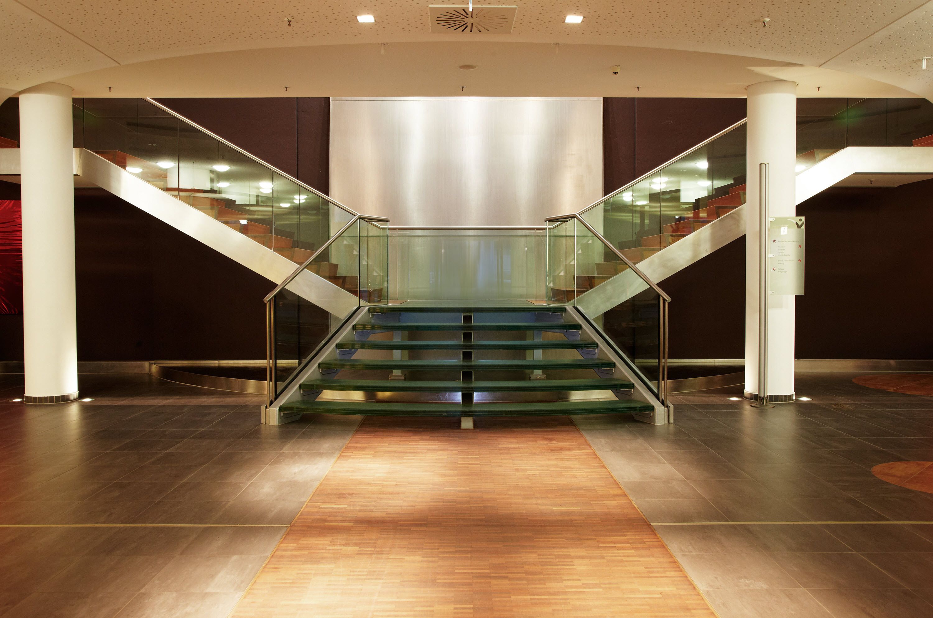 Un interior moderno con una escalera de vidrio y metal, piso de madera pulida y diseño minimalista.
