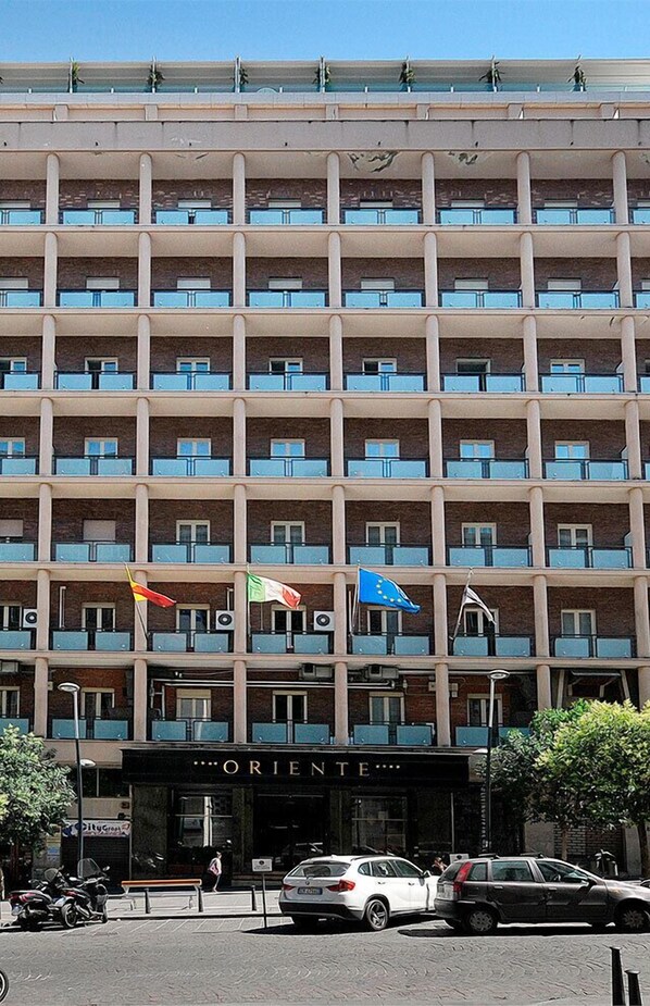 A multi-story hotel with balconies, a storefront labeled "ORIENTE," and flags. - Grand Hotel Oriente (Naples)
