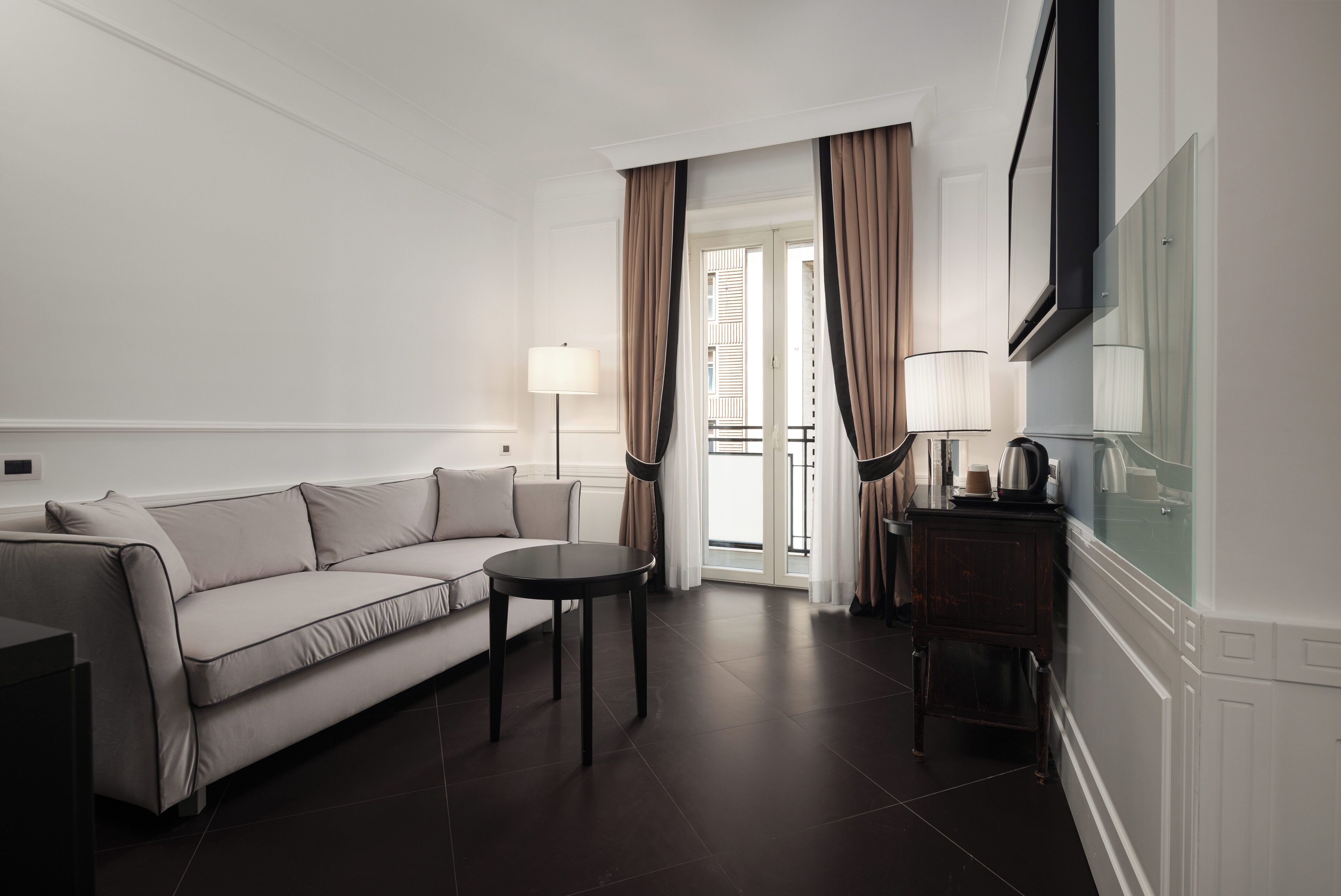 Habitación de hotel con sofá, una mesita redonda, televisor y balcón con cortinas.