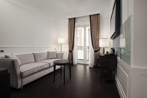 A hotel room with a sofa, a small round table, a TV, and a balcony with curtains. - Grand Hotel Oriente (Naples)